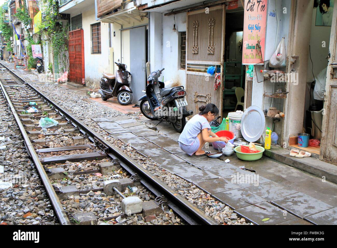 Woman crouching and washing-up near the railway tracks in Hanoi, Vietnam, Asia Stock Photo