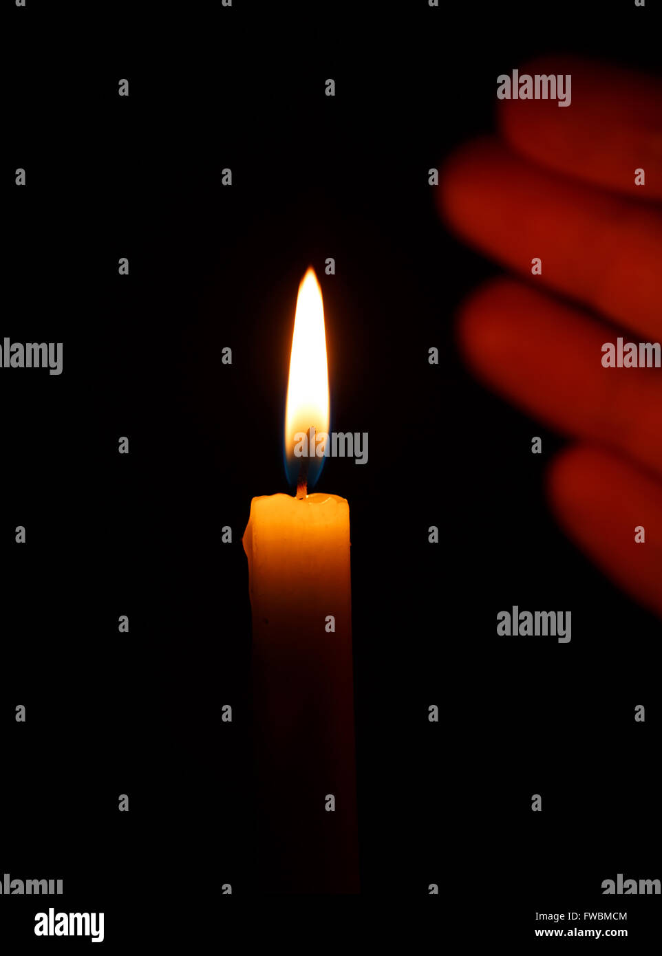 Hand protects the flame of a burning candle on a black background Stock Photo