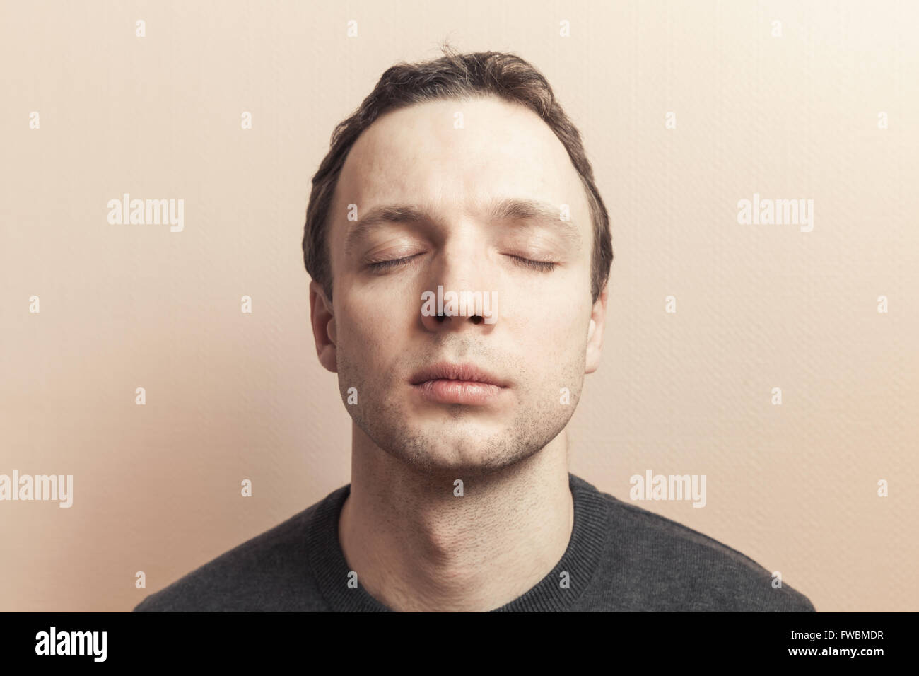 Young Caucasian man with closed eyes. Studio portrait over gray wall background, old style photo filter tonal correction effect Stock Photo