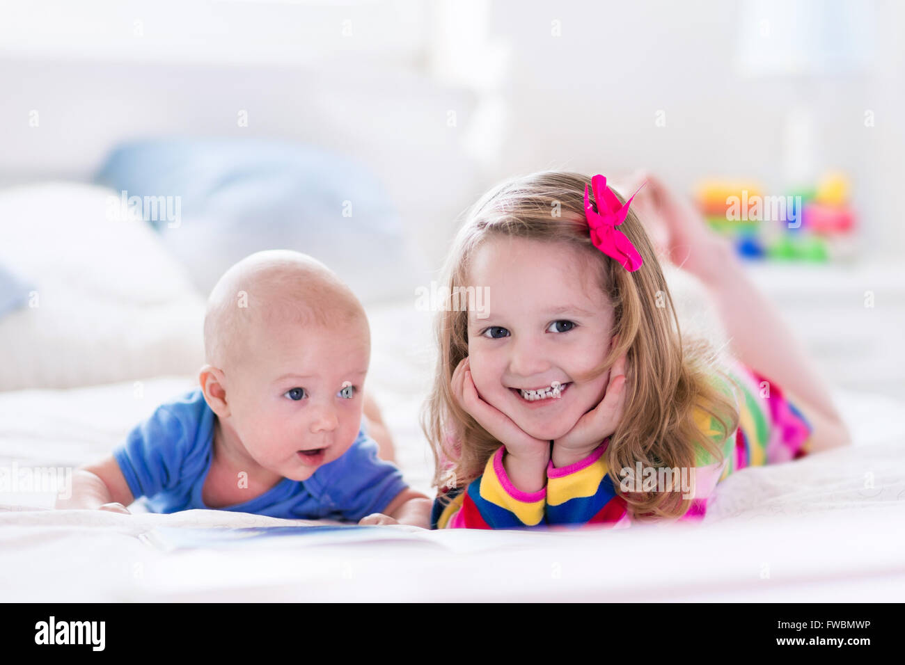 Funny happy toddler girl reading a book and playing with newborn baby