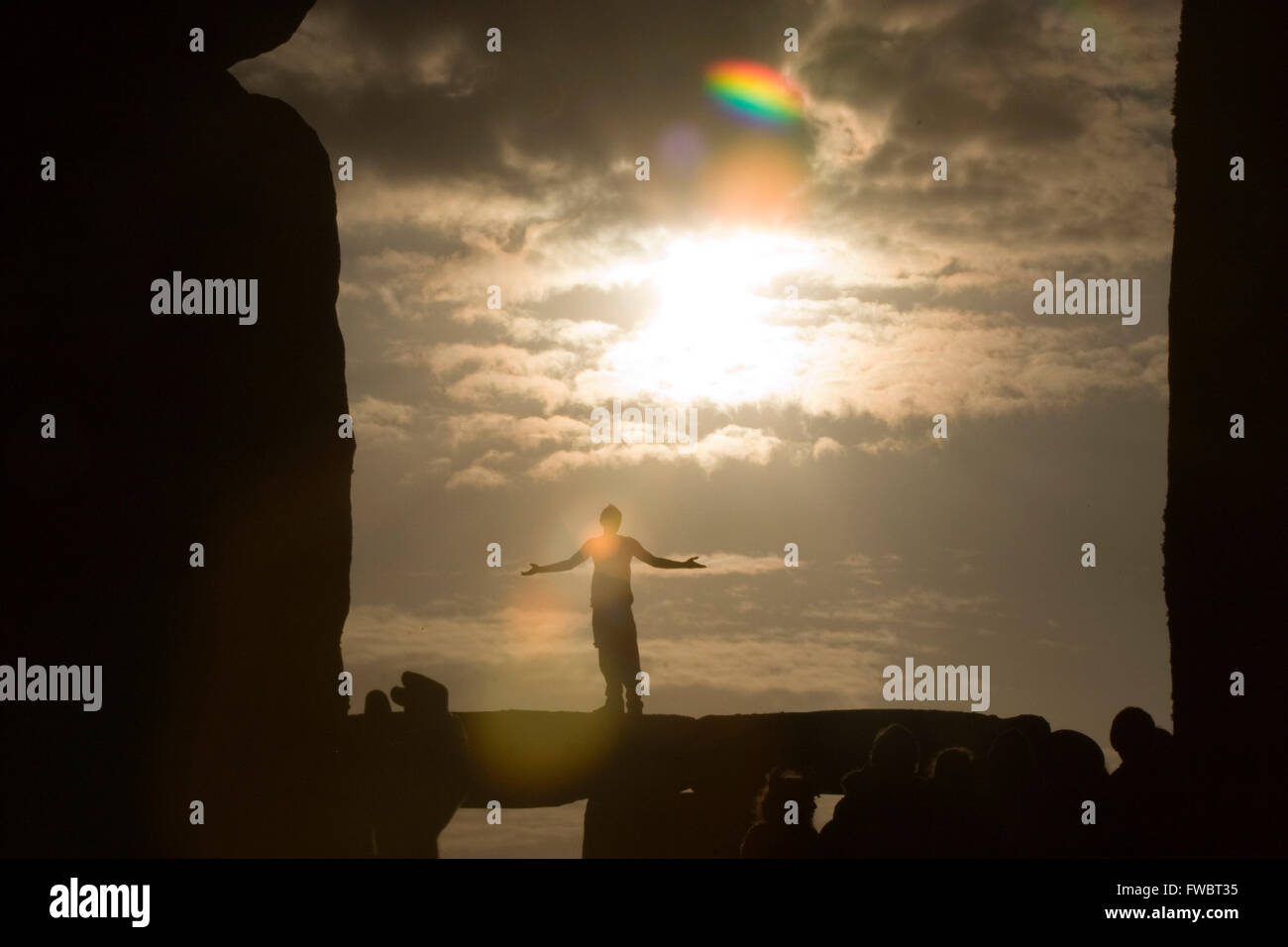 A reveller on top of one of the ancient stones of the Neolithic monument, Stonehenge in the UK as the sunrises ono the morning of the June 21st known as the midsummer solstice. Stock Photo