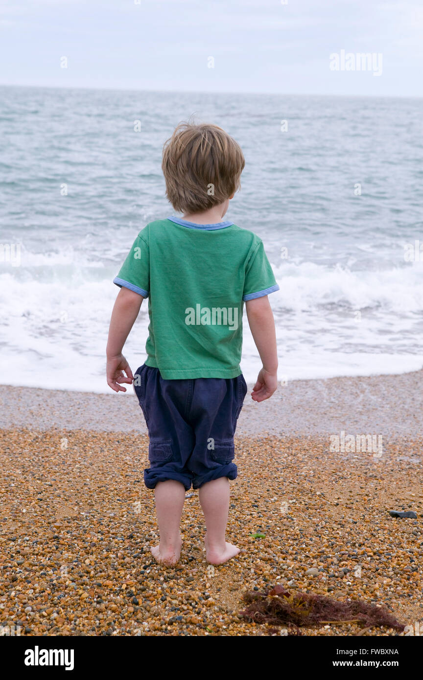 Young boy standing on a pebble beach without shoes and socks looking out to sea Stock Photo Alamy