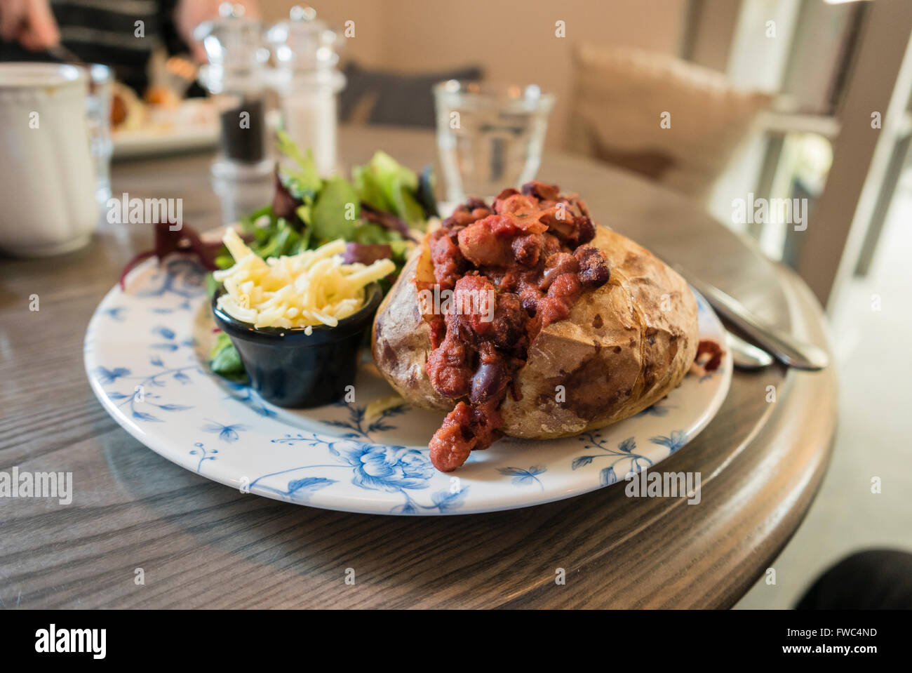 Vegetarian chili-con-carne on a baked jacket potato with vegan cheese and salad in a cafe. Stock Photo