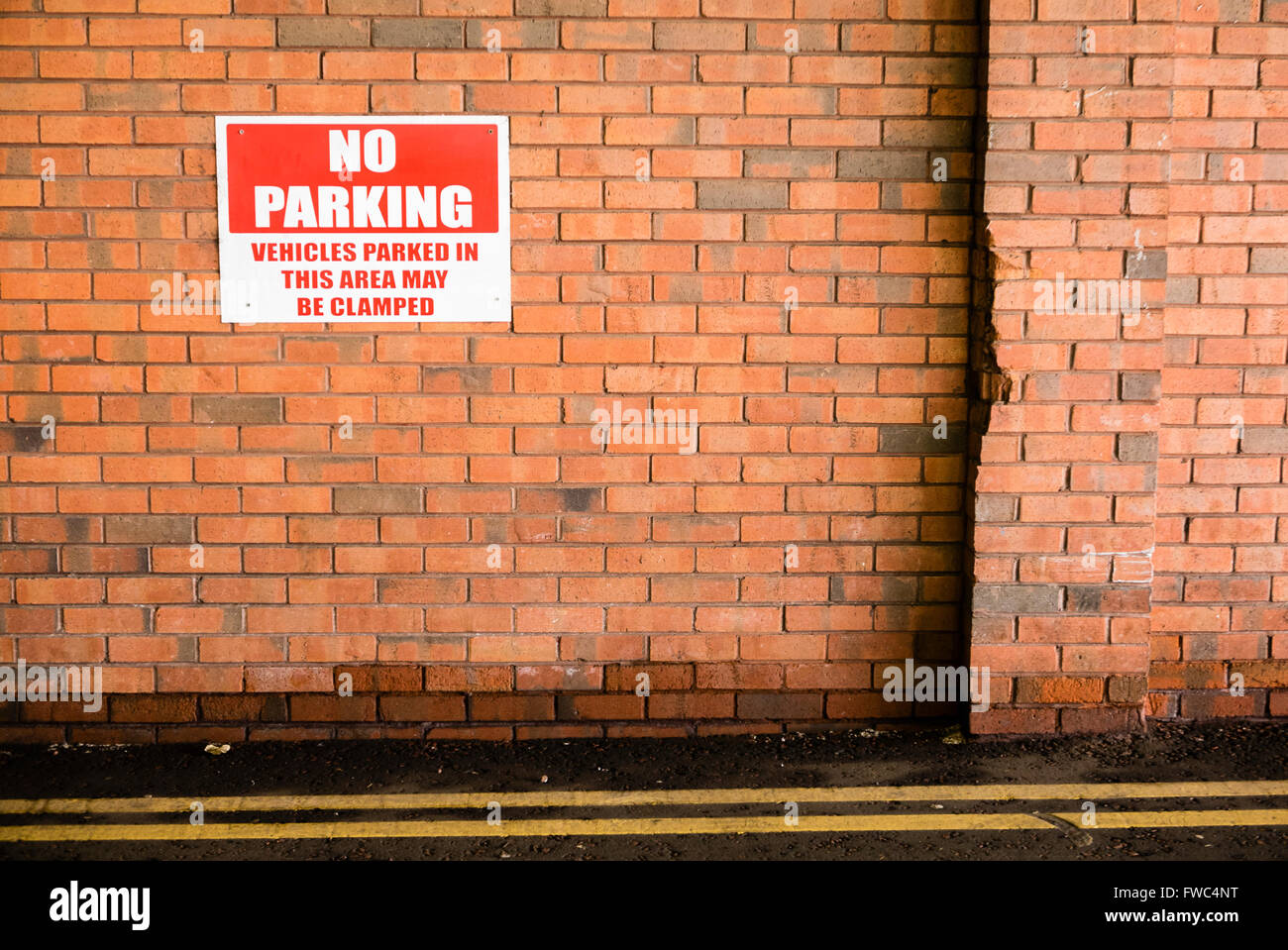 Sign on a brick wall warning that parking is prohibited, and that