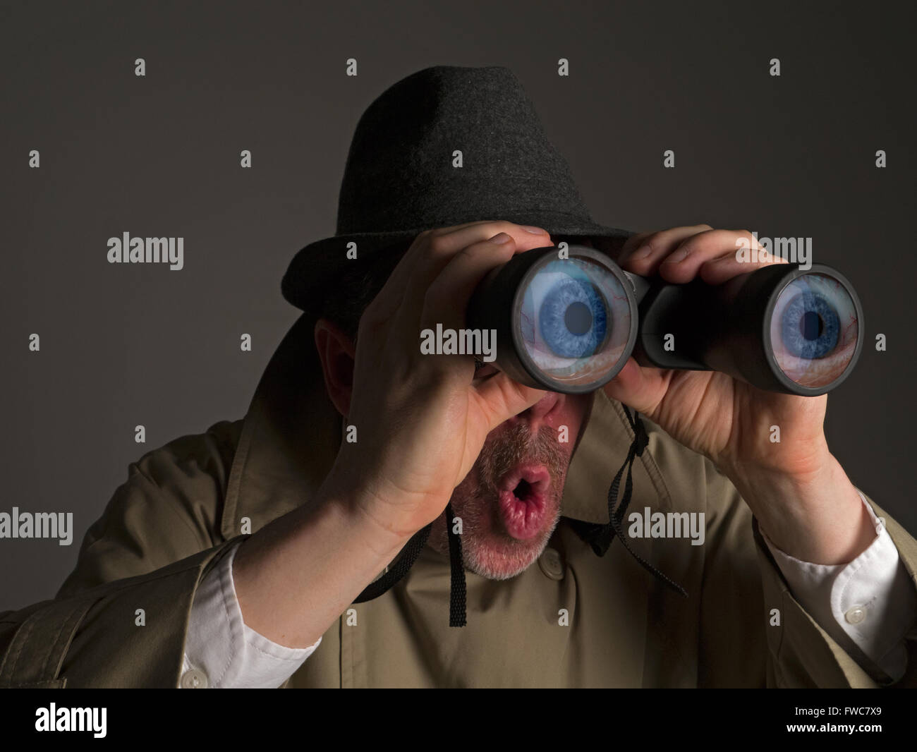 Photograph of a man in trench coat and hat looking through binoculars with huge, cartoonish eyes seen in the lenses. Stock Photo