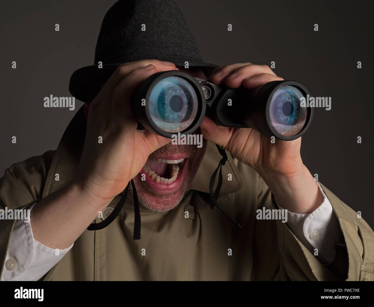 Photograph of a man in trench coat and hat looking through binoculars with huge, cartoonish eyes seen in the lenses. Stock Photo