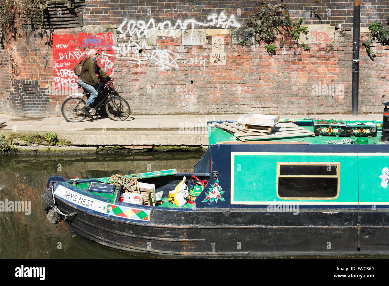 A narrow boat passes a cyclist next to Regent's Canal in London's King's Cross district, England, UK Stock Photo
