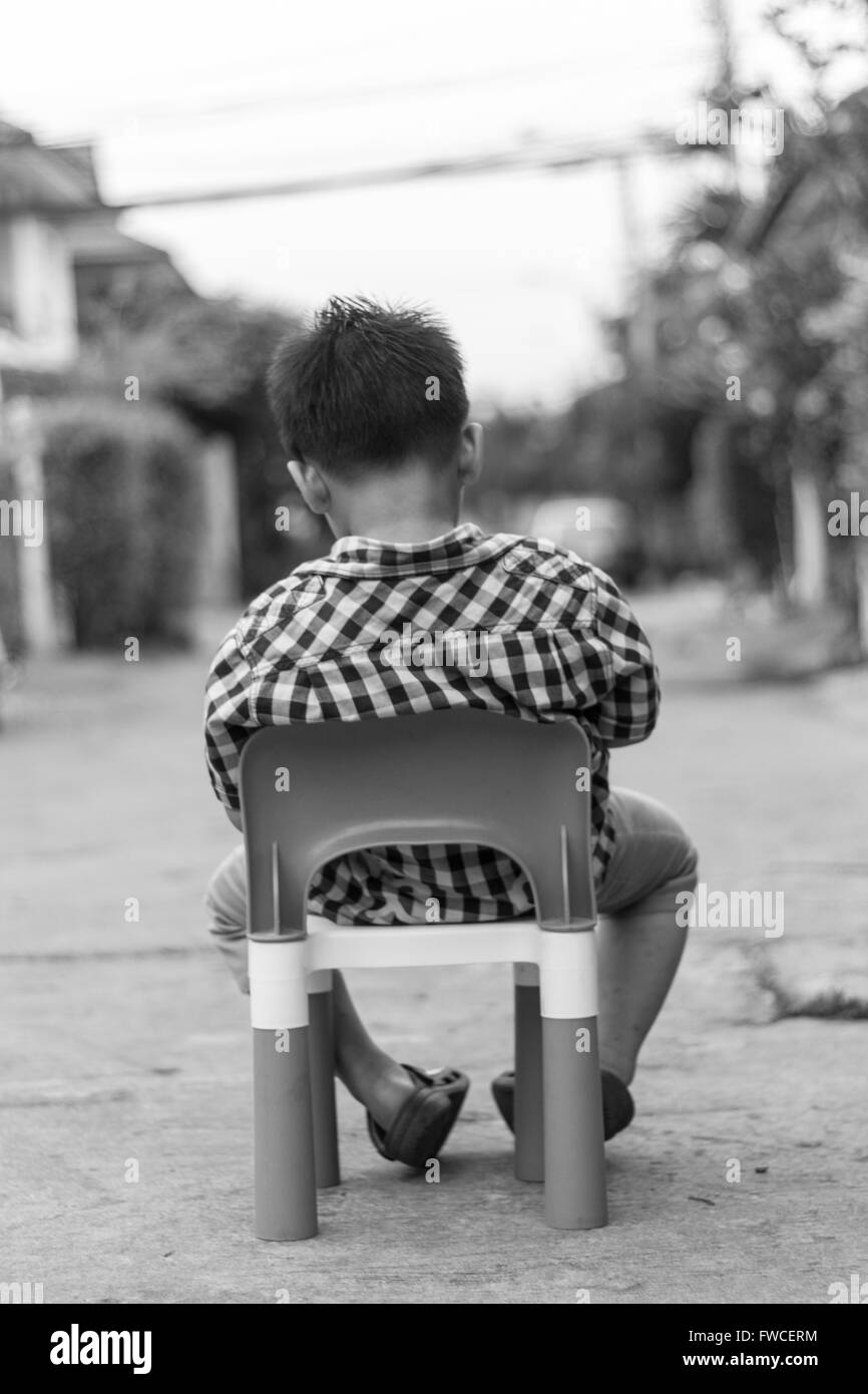 Alone boy sit on the plastic chair on the concrete road Stock Photo