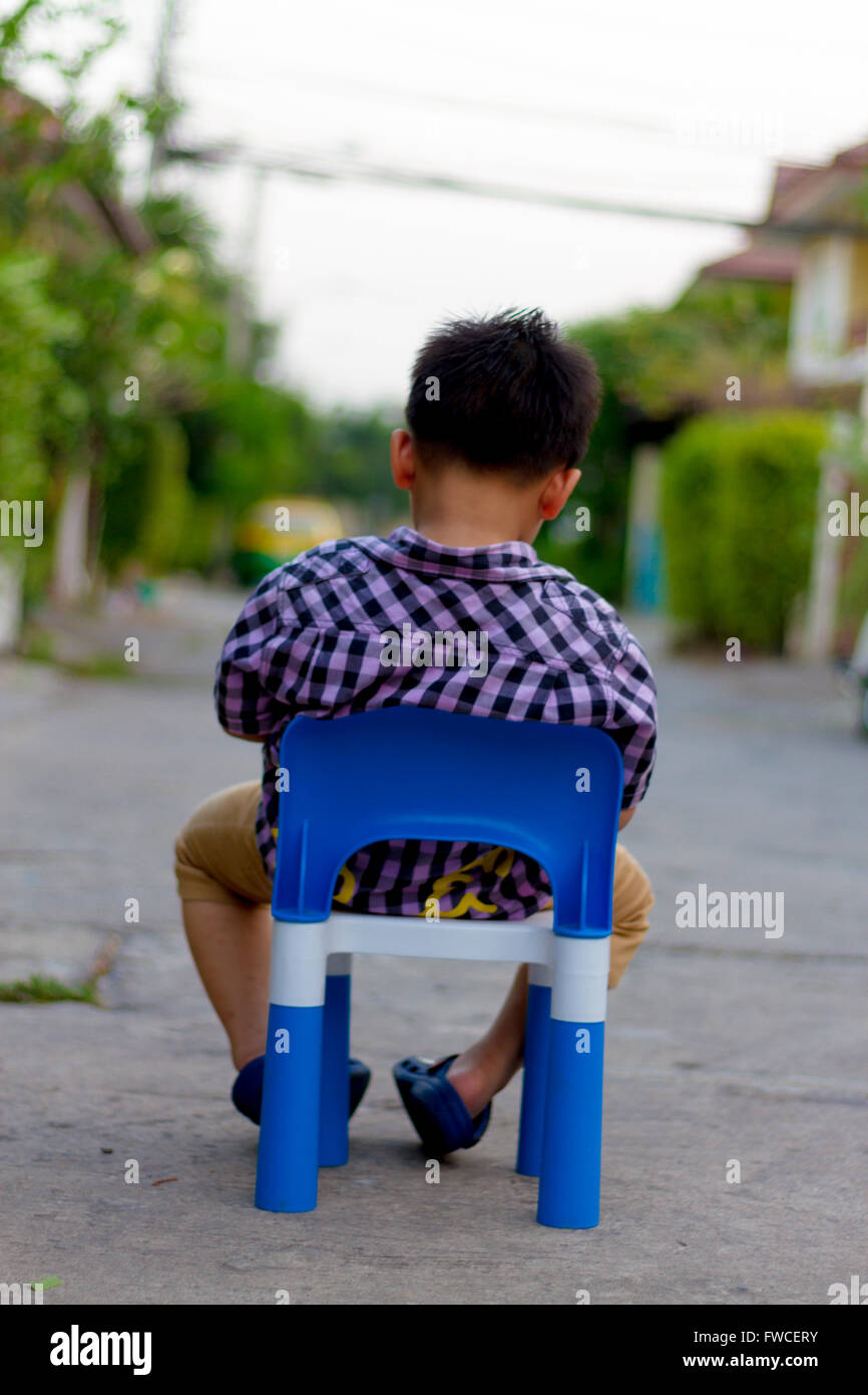 Alone boy sit on the plastic chair on the concrete road Stock Photo