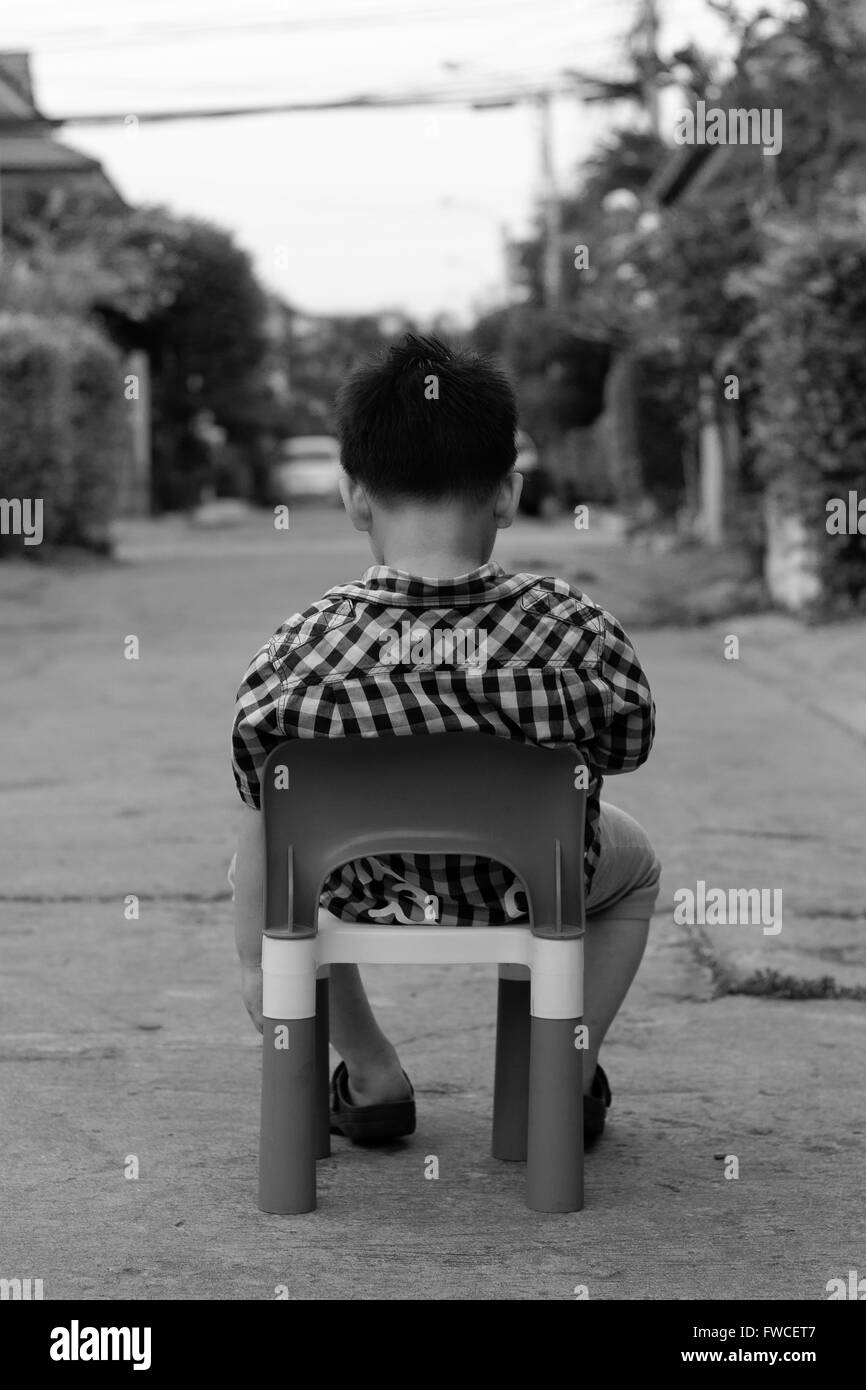 Alone boy sit on the plastic chair on the concrete road Stock Photo