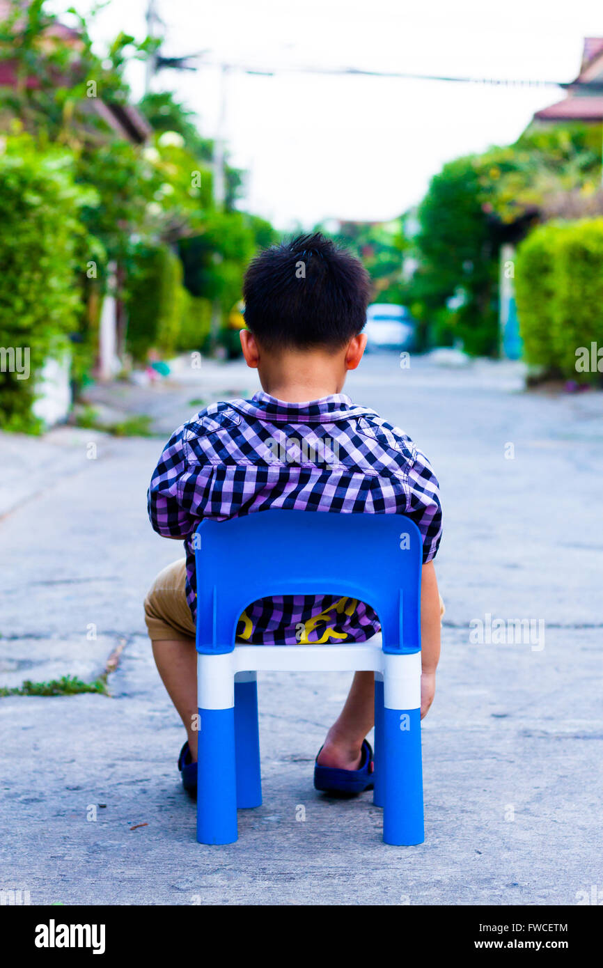 Alone boy sit on the plastic chair on the concrete road Stock Photo