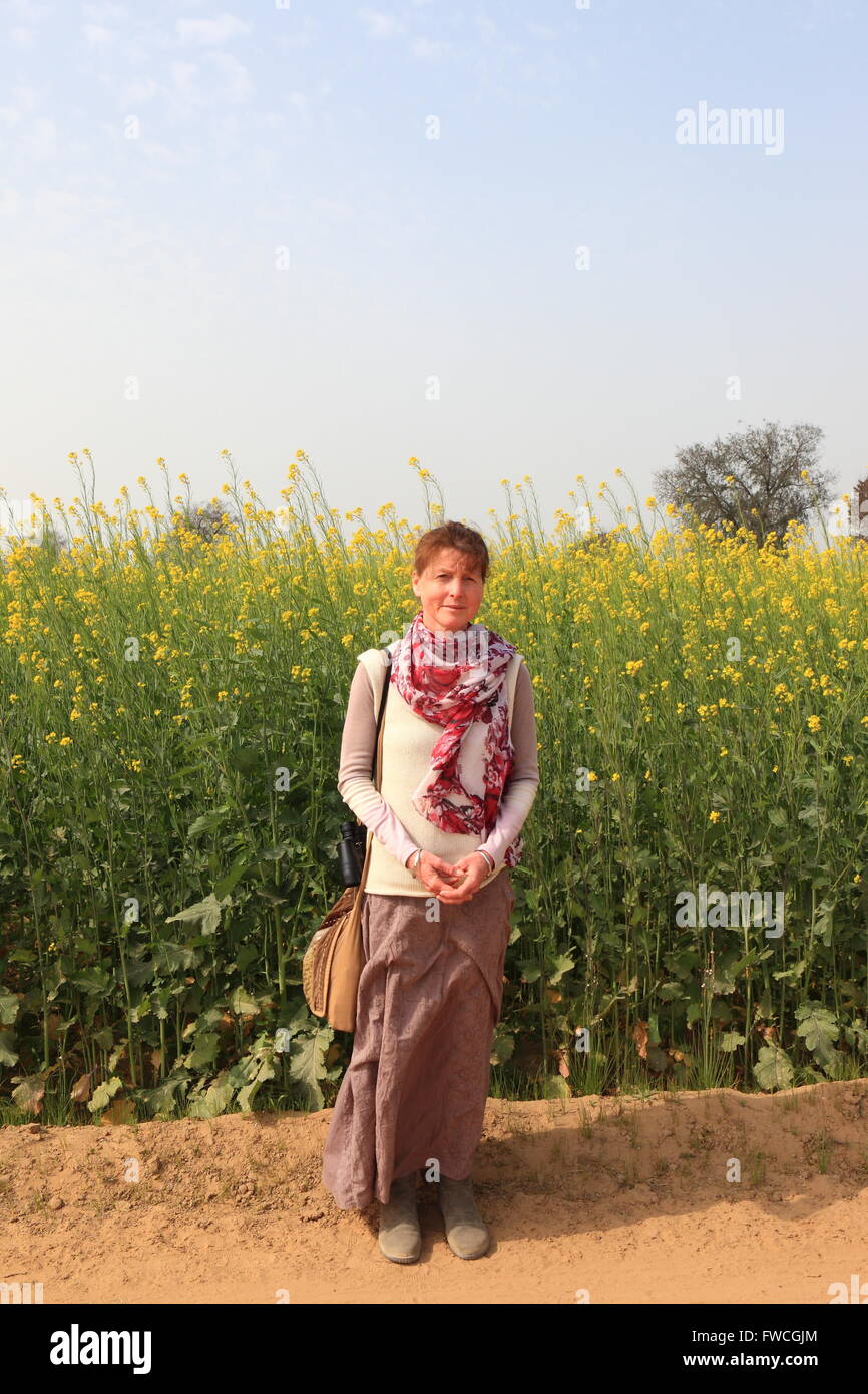 A western lady tourist walks along a dusty track between flowering mustard fields in Abohar rural, Ferozepur district, Rajasthan Stock Photo
