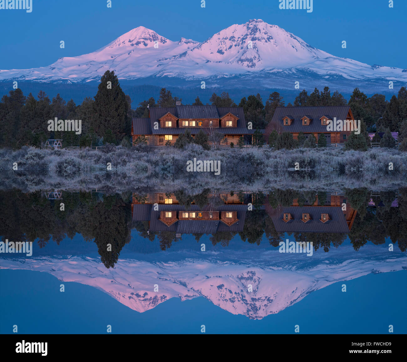USA, Oregon, Deschutes County, Central Oregon, Cascade Mountains, Sisters, Log home and Three Sisters reflected in pond Stock Photo
