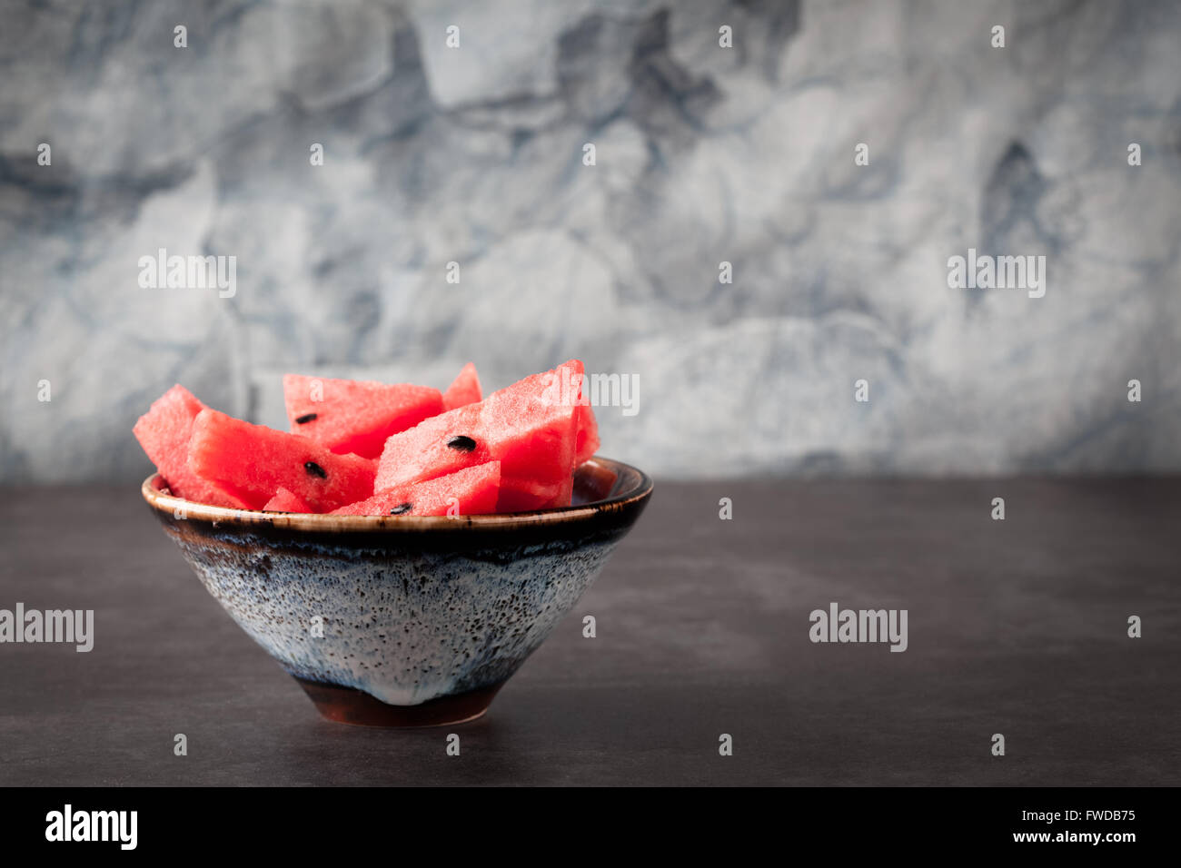 Sliced watermelon in handmade ceramic bowl on blurred  background with copy space. Shallow depth of field. Stock Photo
