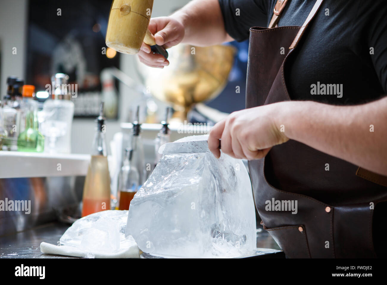 Bartender mannually crushed ice with wooden hammer and metal knife. Stock Photo