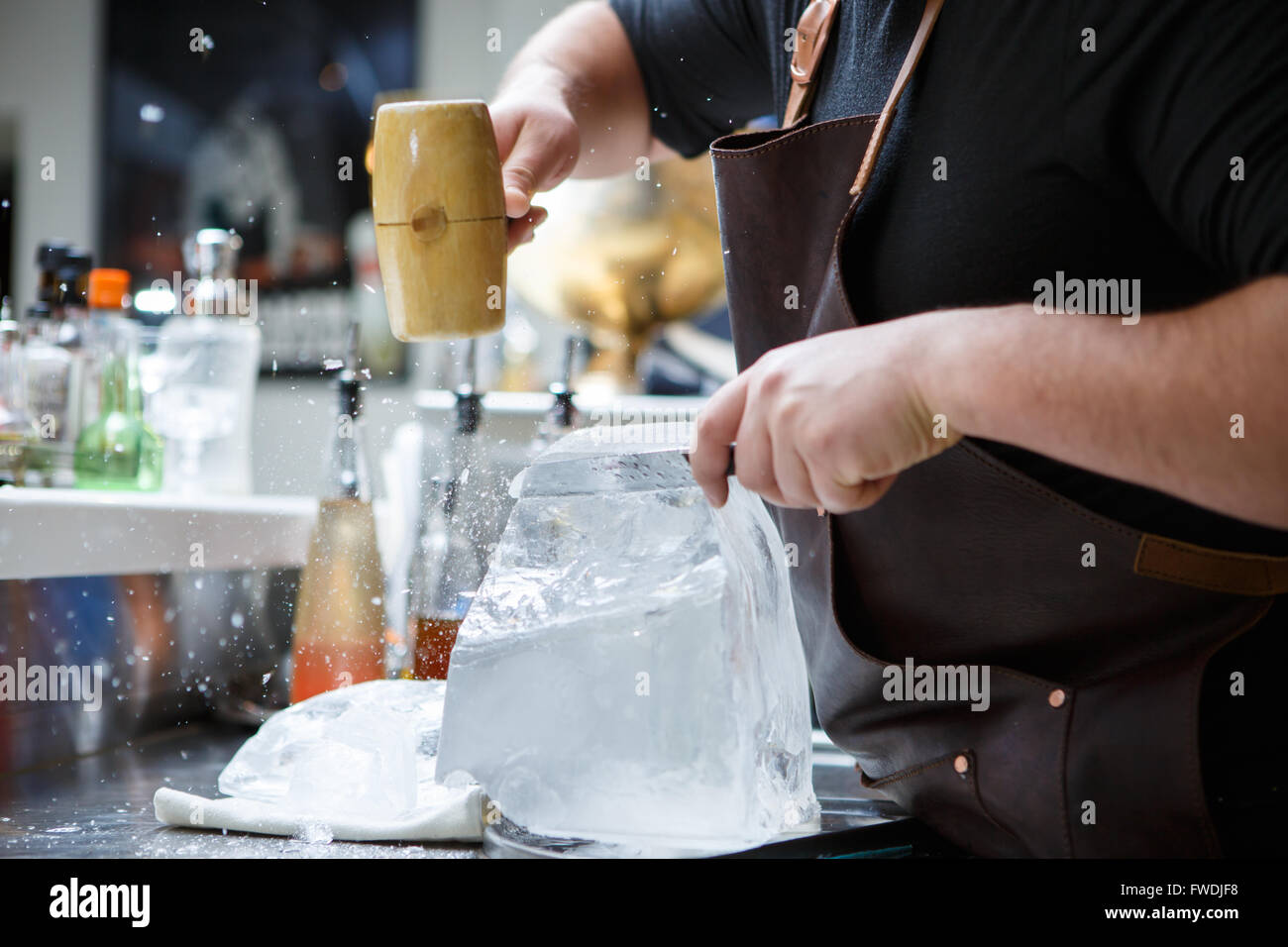 Bartender mannually crushed ice with wooden hammer and metal knife. Stock Photo