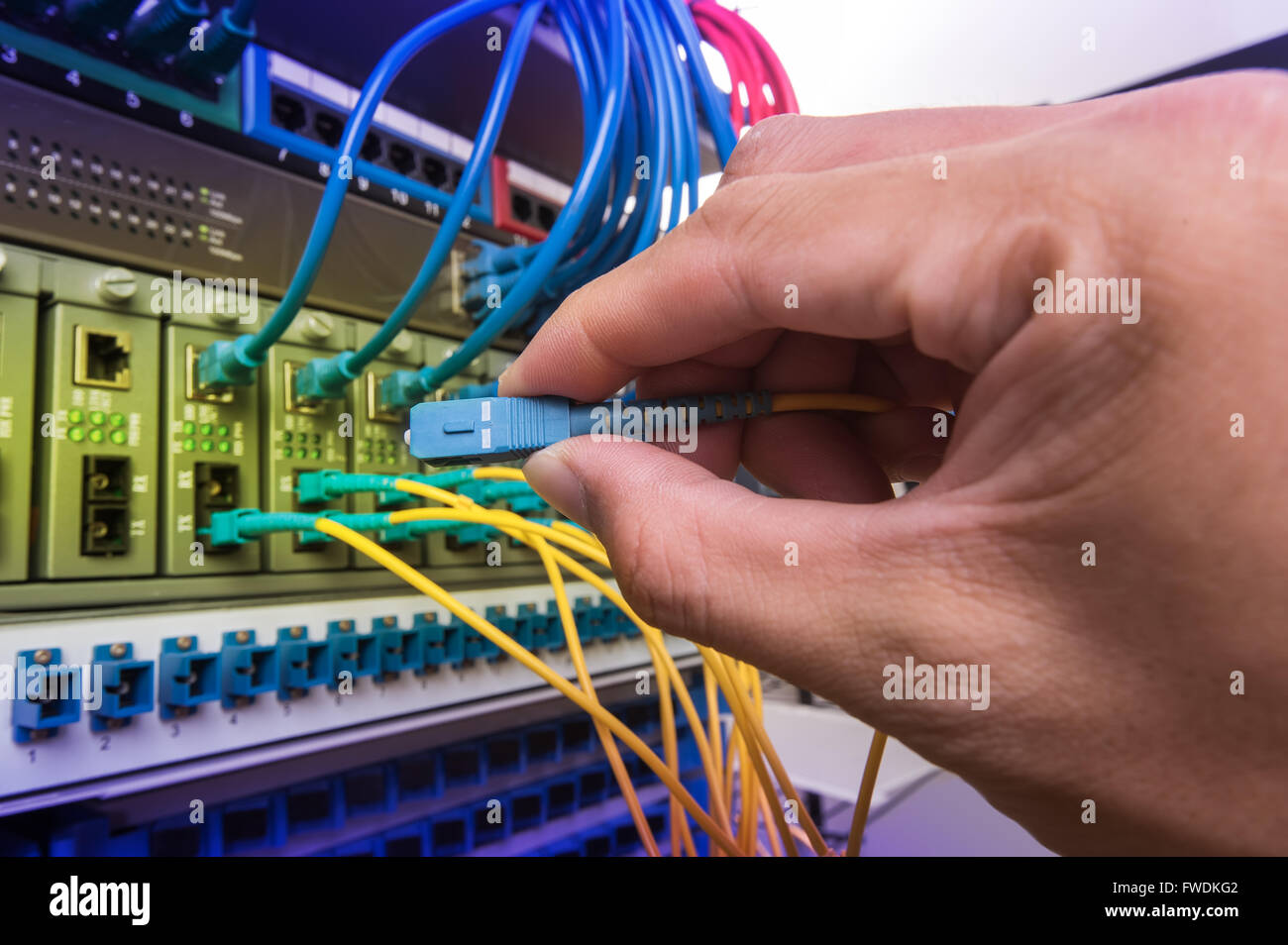 man working in network server room with fiber optic hub for digital ...