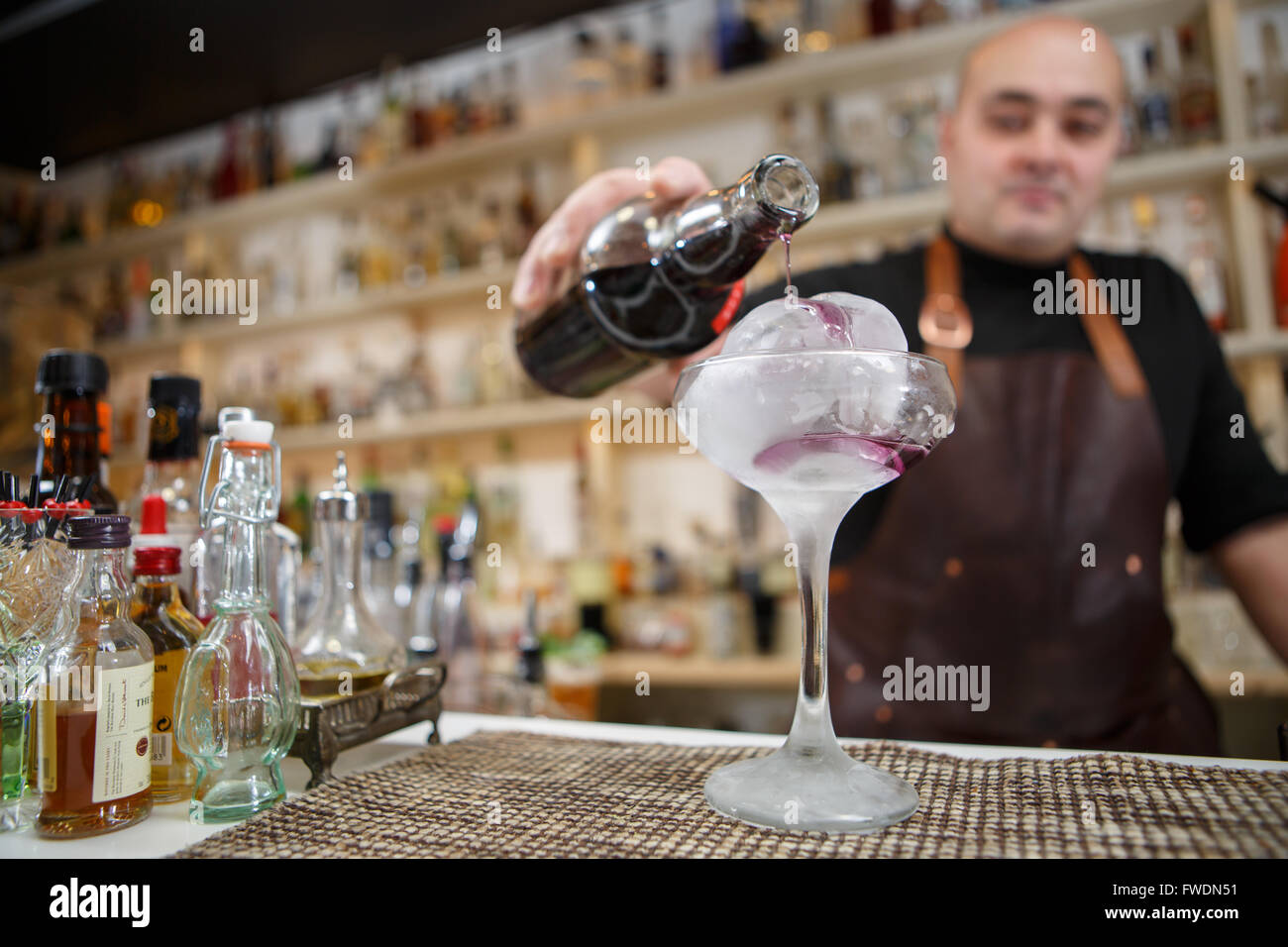 Bartender is pouring wine in the glass with giant ice, wide-angle image. Stock Photo