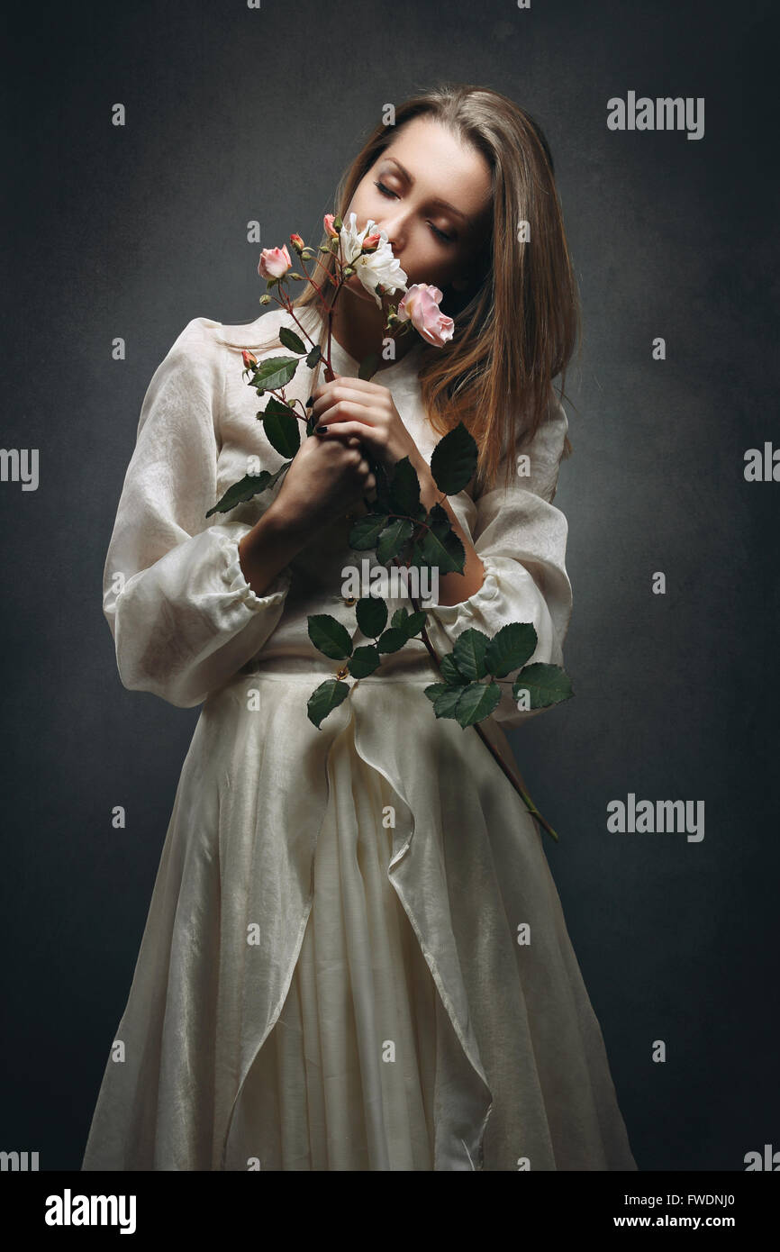 Beautiful woman with victorian dress smelling flowers fragrance . Purity concept Stock Photo