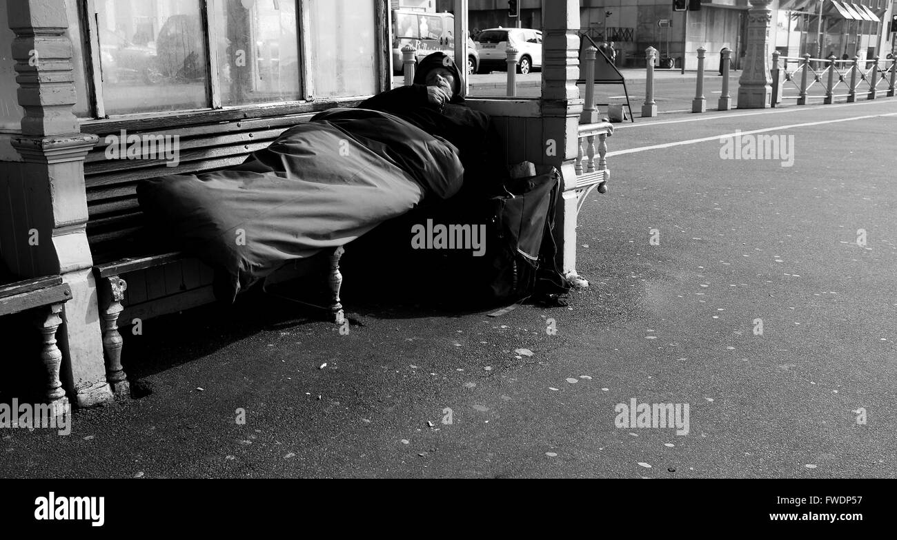 Homeless man asleep in sleeping bag in seafront shelter Brighton UK
