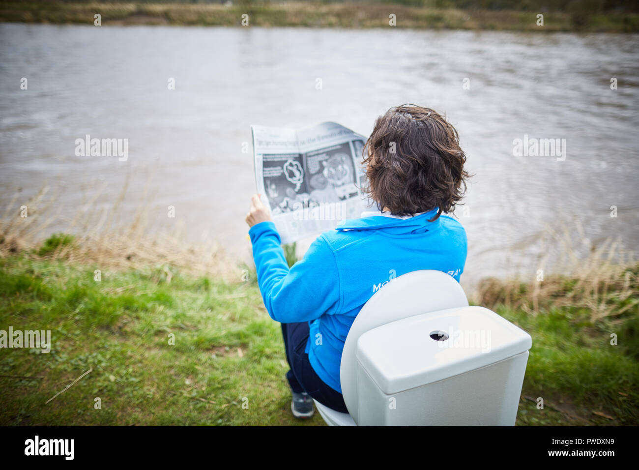 Sat on a toilet reading newspaper loo potty urinal sitting using sewage Stock Photo