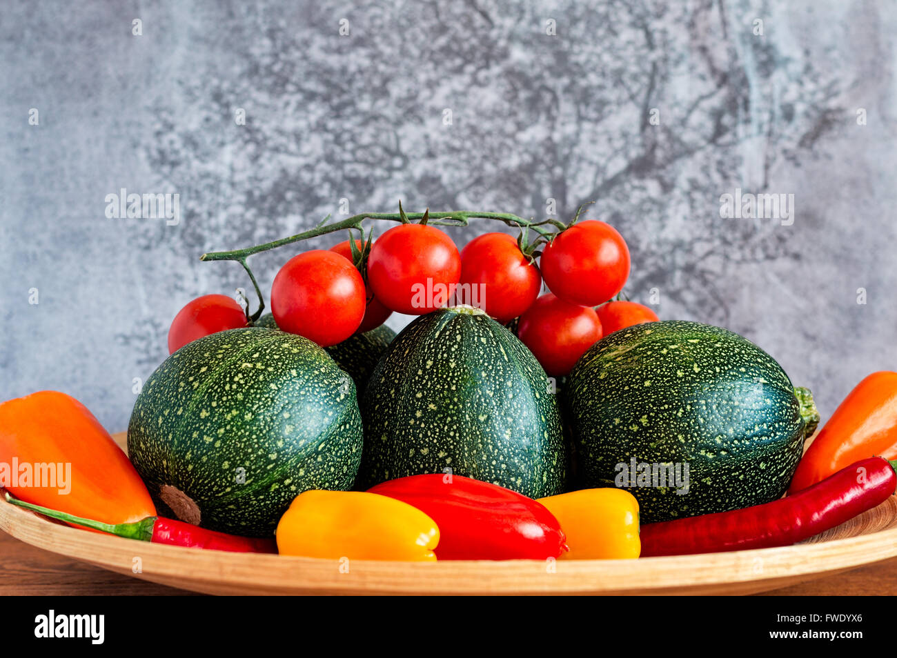 Selection of eight ball zucchini, cherry tomatoes, chili peppers and yellow, orange and red peppers on a bamboo plate. Stock Photo