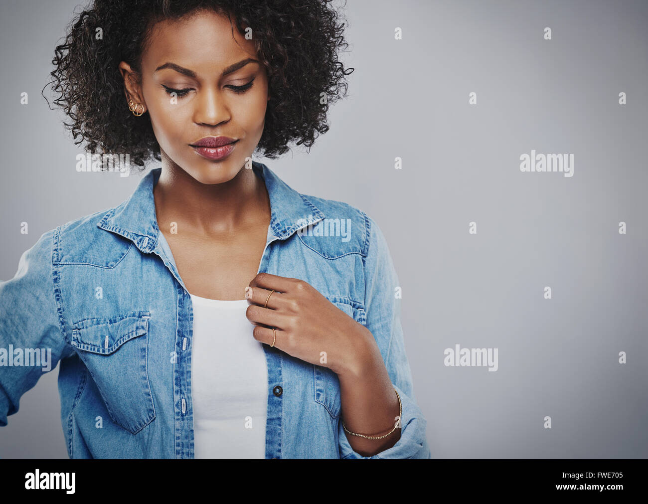 Thoughtful attractive young African American woman wearing a casual denim jacket standing with downcast eyes looking down at the Stock Photo