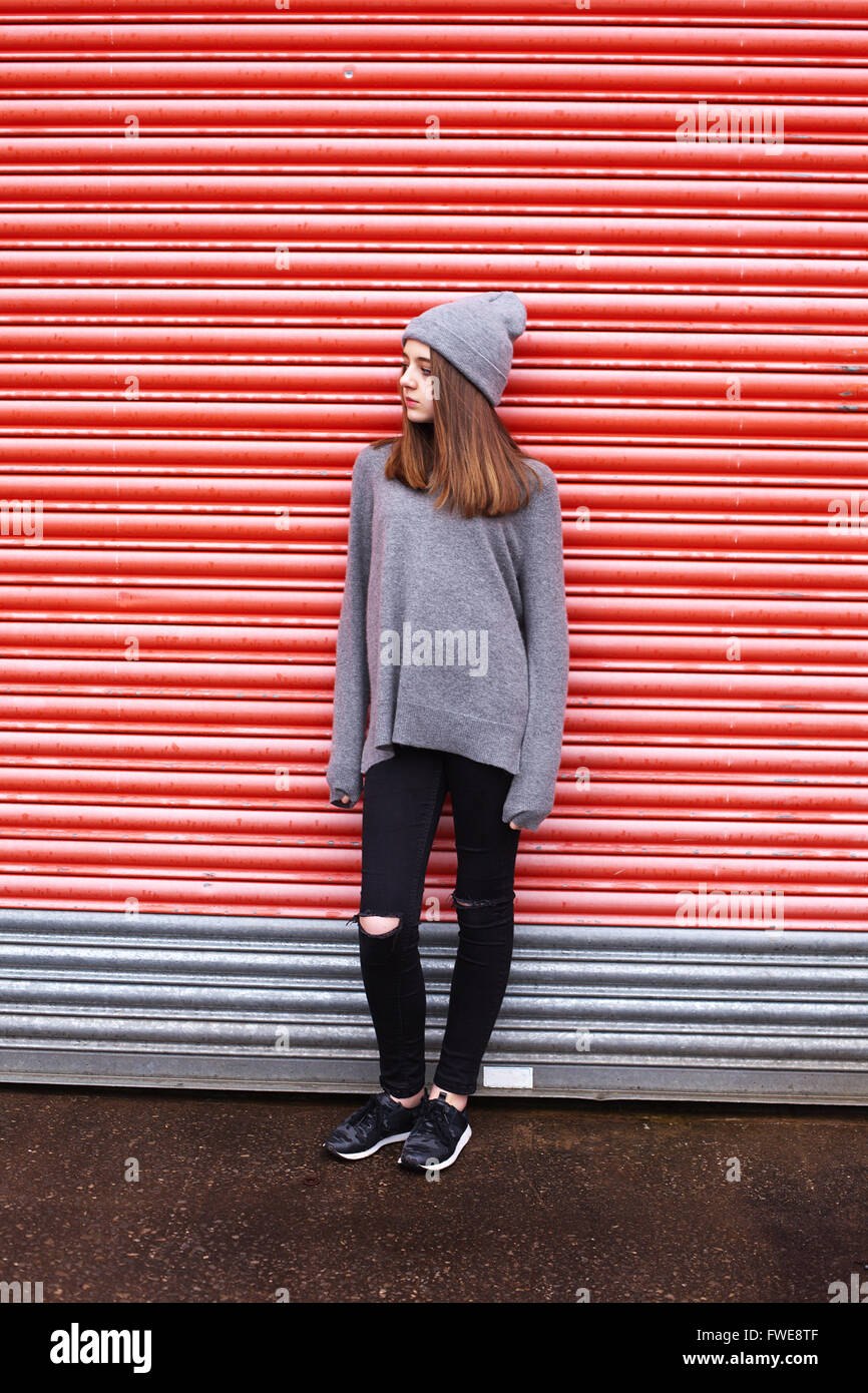 Teenage girl leaning against a shuttered door in an urban environment Stock Photo