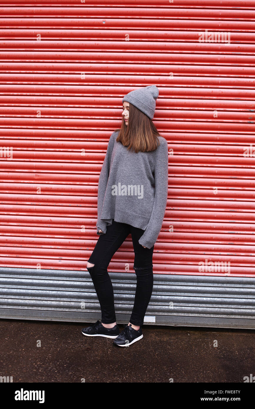 Teenage girl leaning against a shuttered door in an urban environment Stock Photo