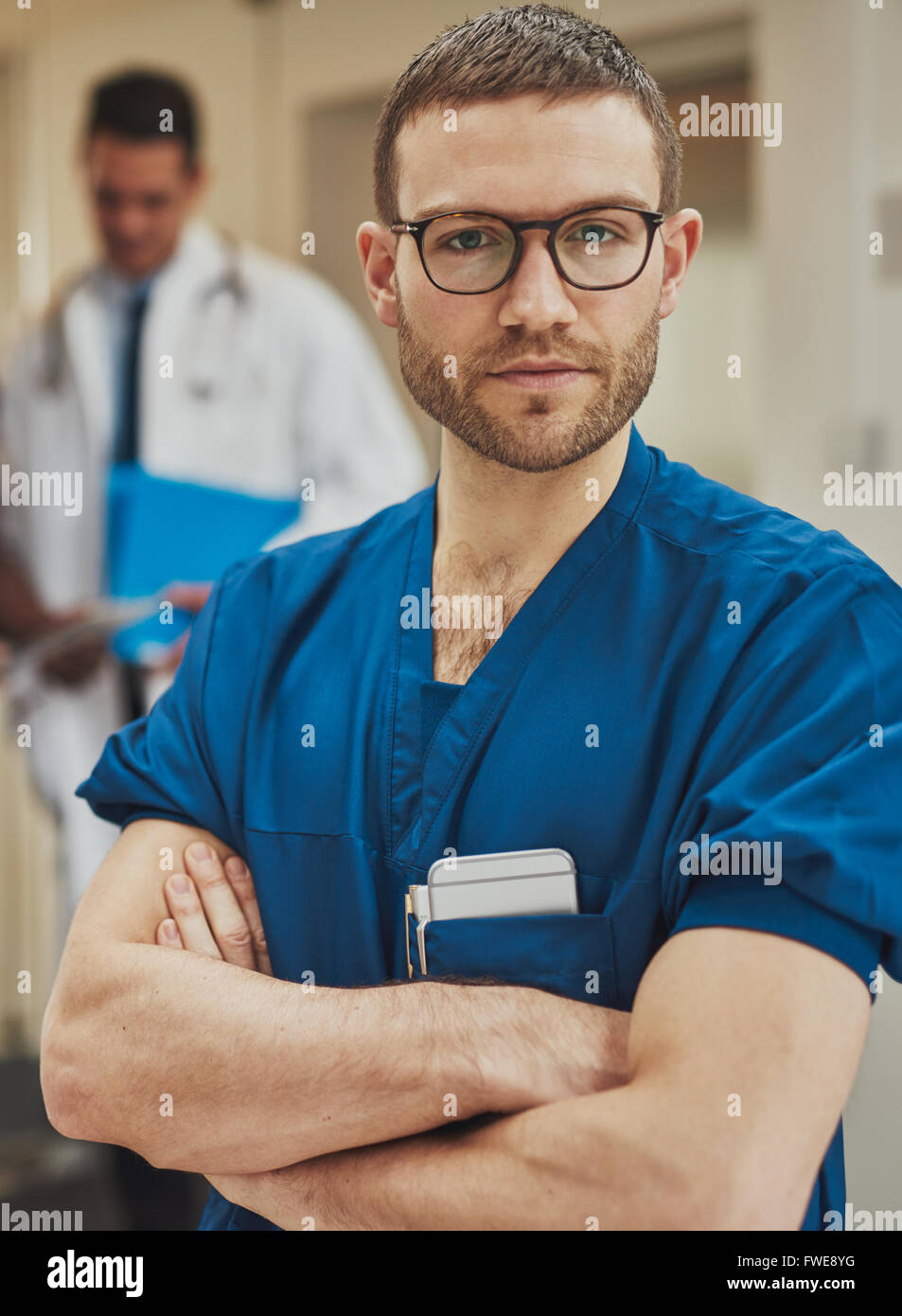 Serious confident young surgeon wearing glasses and surgical scrubs