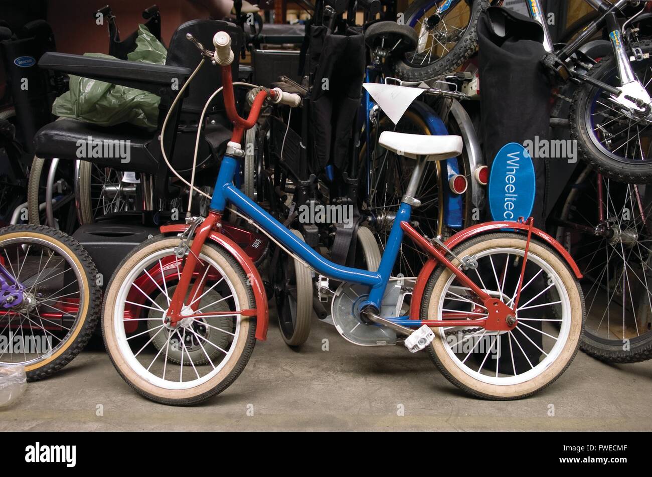 Much Hoole, Preston, Lancashire. A restored hand painted child's bike in blue and red, sits in the warehouse at the International Aid Trust charity shop. The charity raise funds and aid for humanitarian causes across the globe. Stock Photo