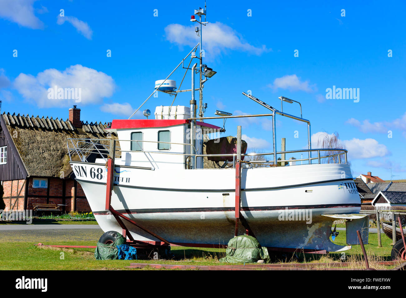Kivik, Sweden - April 1, 2016: White fishing boat on trailer in a fishing community. House and cloudy sky in background. Stock Photo