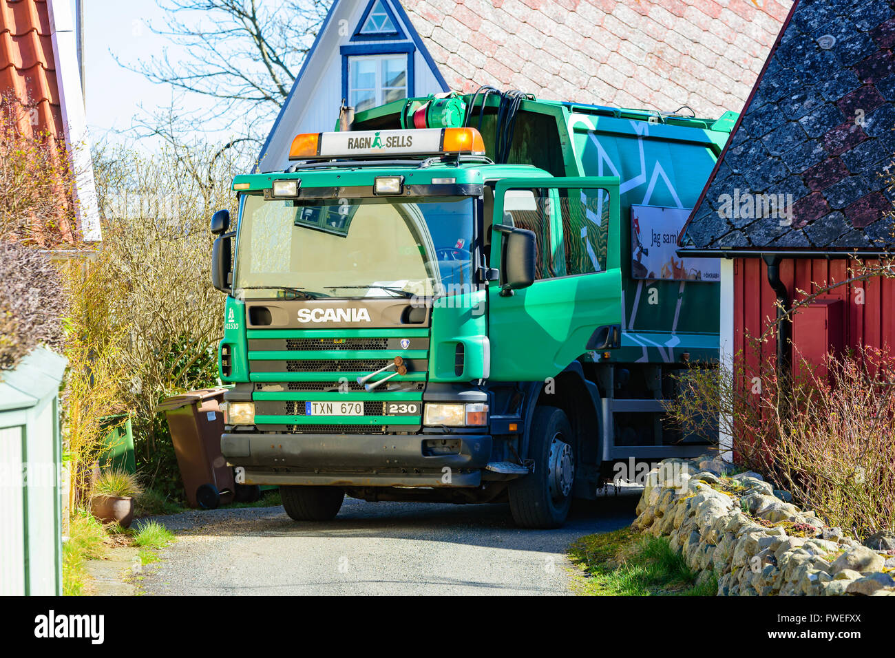 Kivik, Sweden - April 1, 2016: A green Scania 230 garbage truck stand in a tight fit between houses while collecting household g Stock Photo