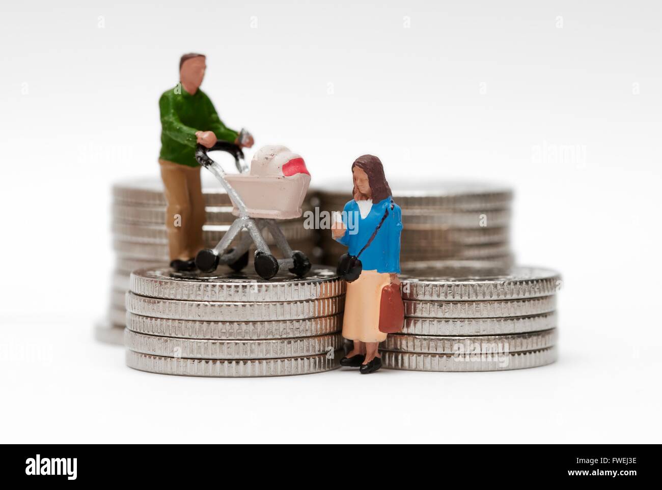 A miniature figurine married couple with a pram standing on silver colored coins Stock Photo