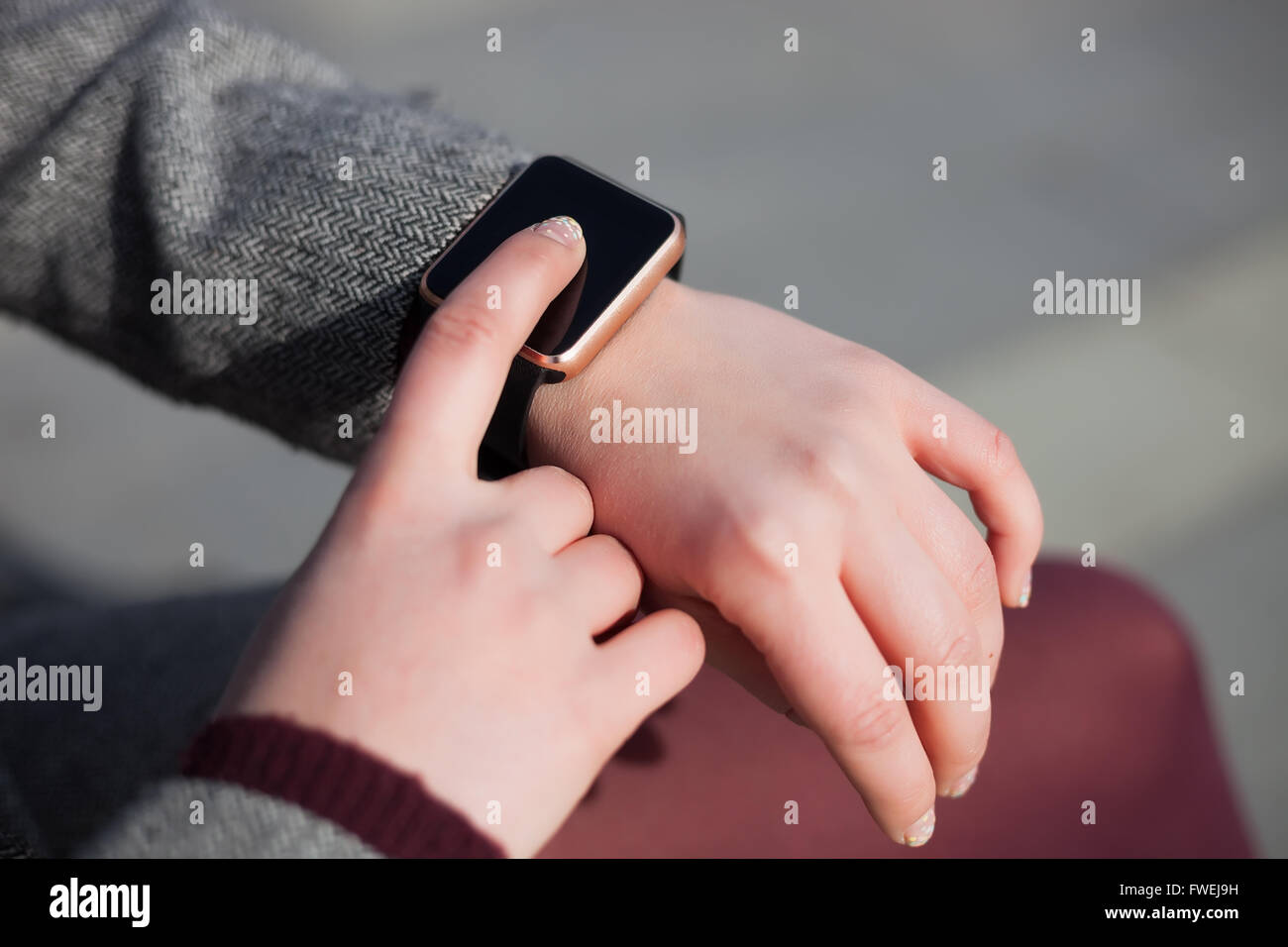 Woman in grey coat and marsala tights using her trendy smart wrist watch. This person is always connected to social media and internet. Stock Photo