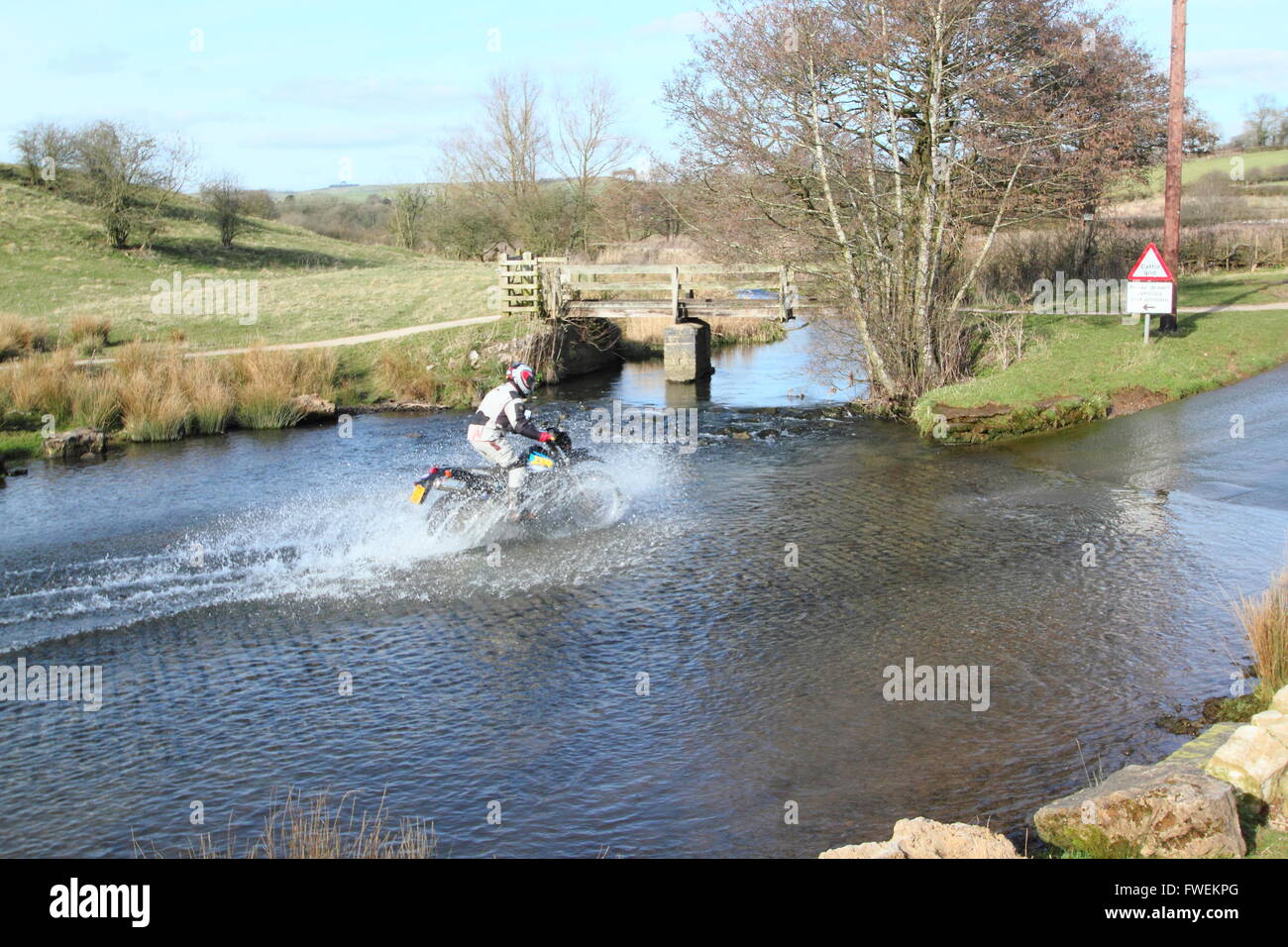 A motor cyclist navigates  Bradbourne Brook at the Tissington Ford at Tissington in the Derbyshire Dales, England UK Stock Photo