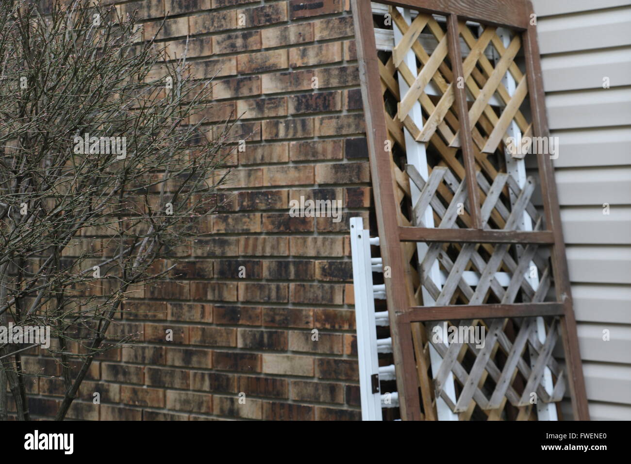 Criss-crossed wood paneling leans against a brick-walled house in winter. Stock Photo
