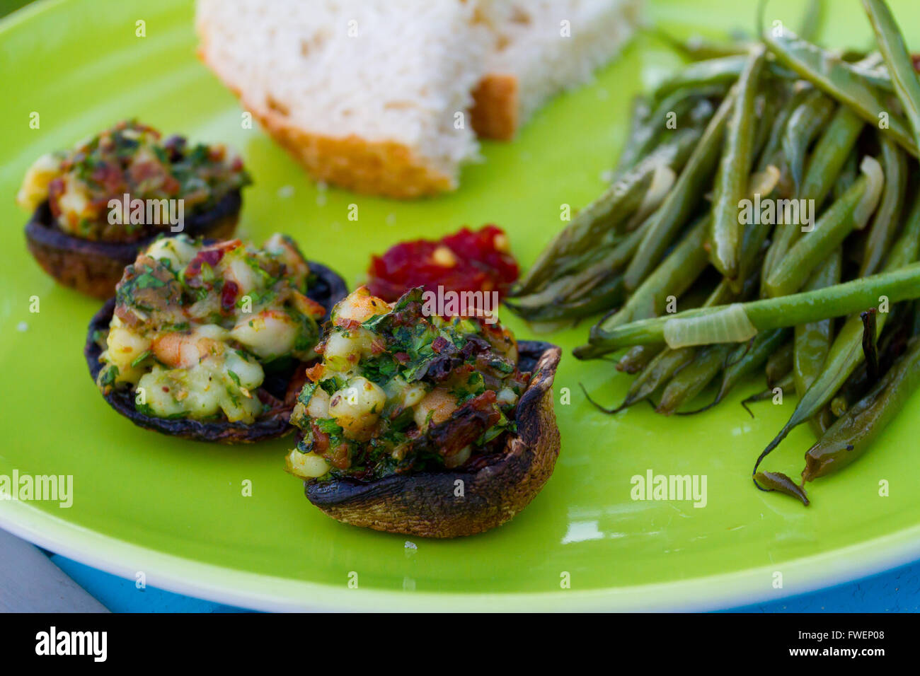 This gourmet meal of stuffed mushrooms and green beans served on a green plate with some white bread. This is dinner but the ima Stock Photo