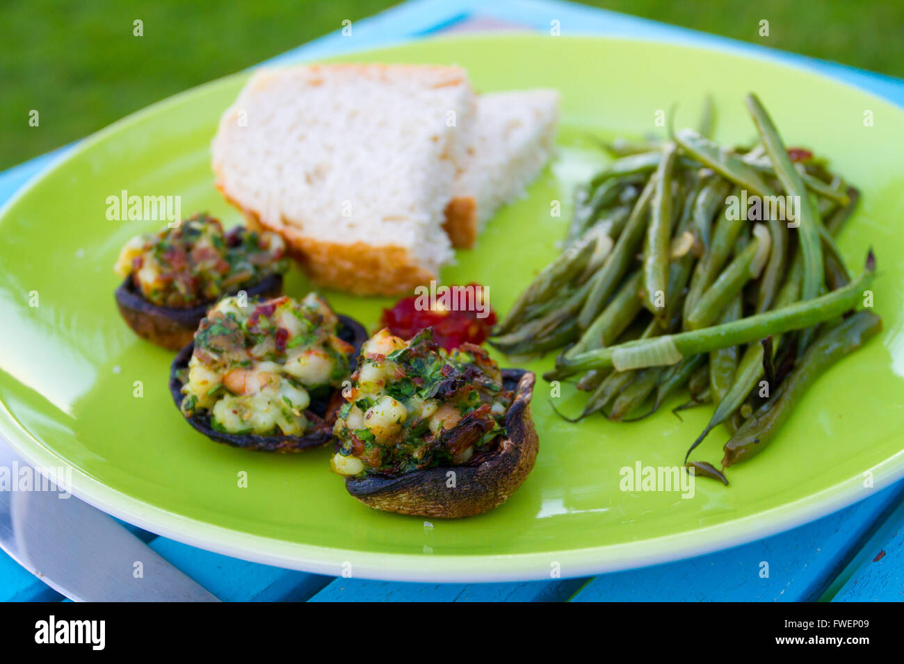 This gourmet meal of stuffed mushrooms and green beans served on a green plate with some white bread. This is dinner but the ima Stock Photo
