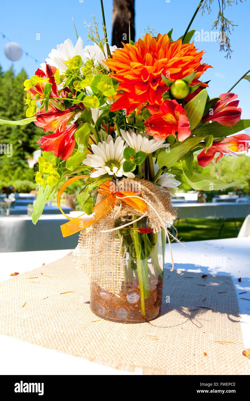 White, orange, and green wedding flower arrangements with burlap as the