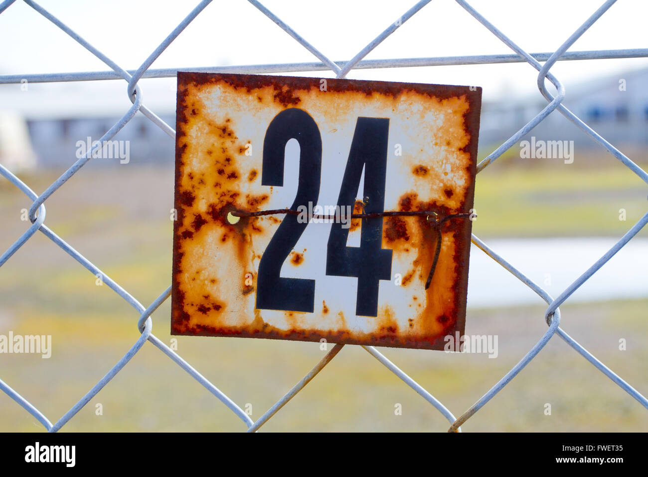 A series of rusted old signs or tags are attached to this chain link fence with orange and white rust and the numbers clearly vi Stock Photo