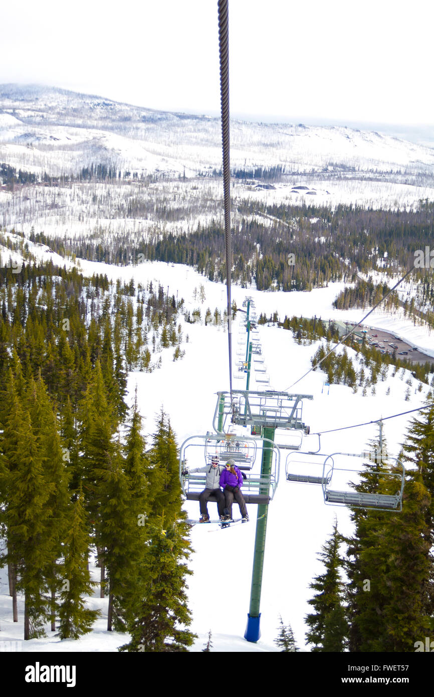 A couple of people ride the ski chair lift up the mountain together while sitting closely to each other having a fun time during Stock Photo