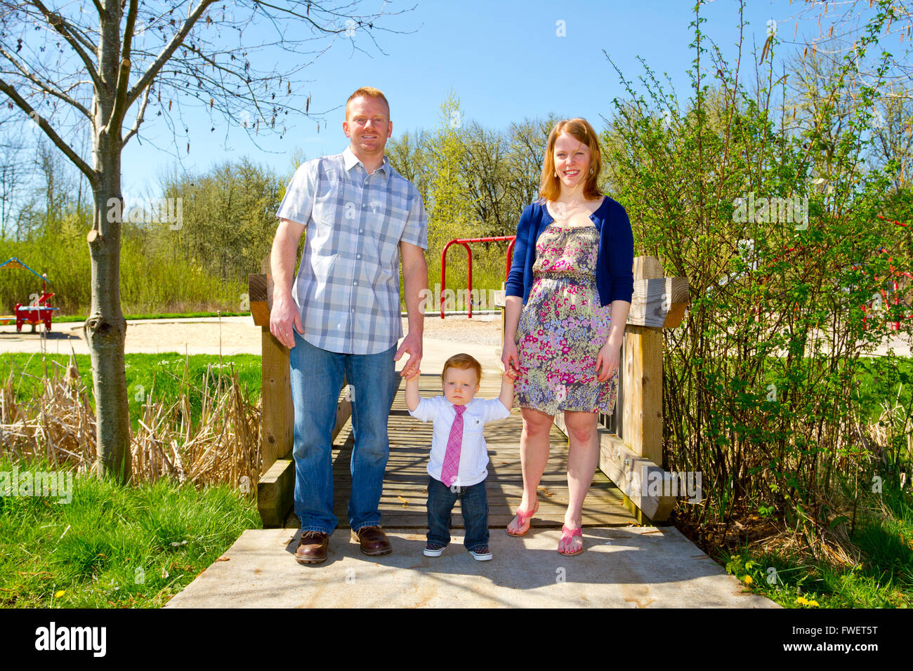 A man and a woman hold their baby one year old son while posing for a family photo outdoors. Stock Photo