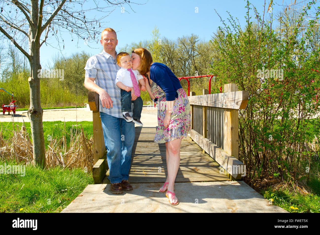 A man and a woman hold their baby one year old son while posing for a family photo outdoors. Stock Photo