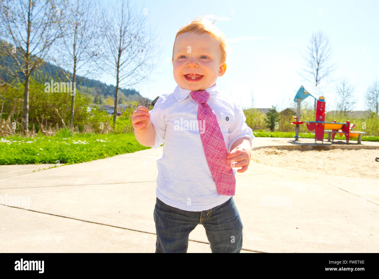 A baby boy plays at the park wearing his Sunday's best clothes including a tie around his neck. Stock Photo
