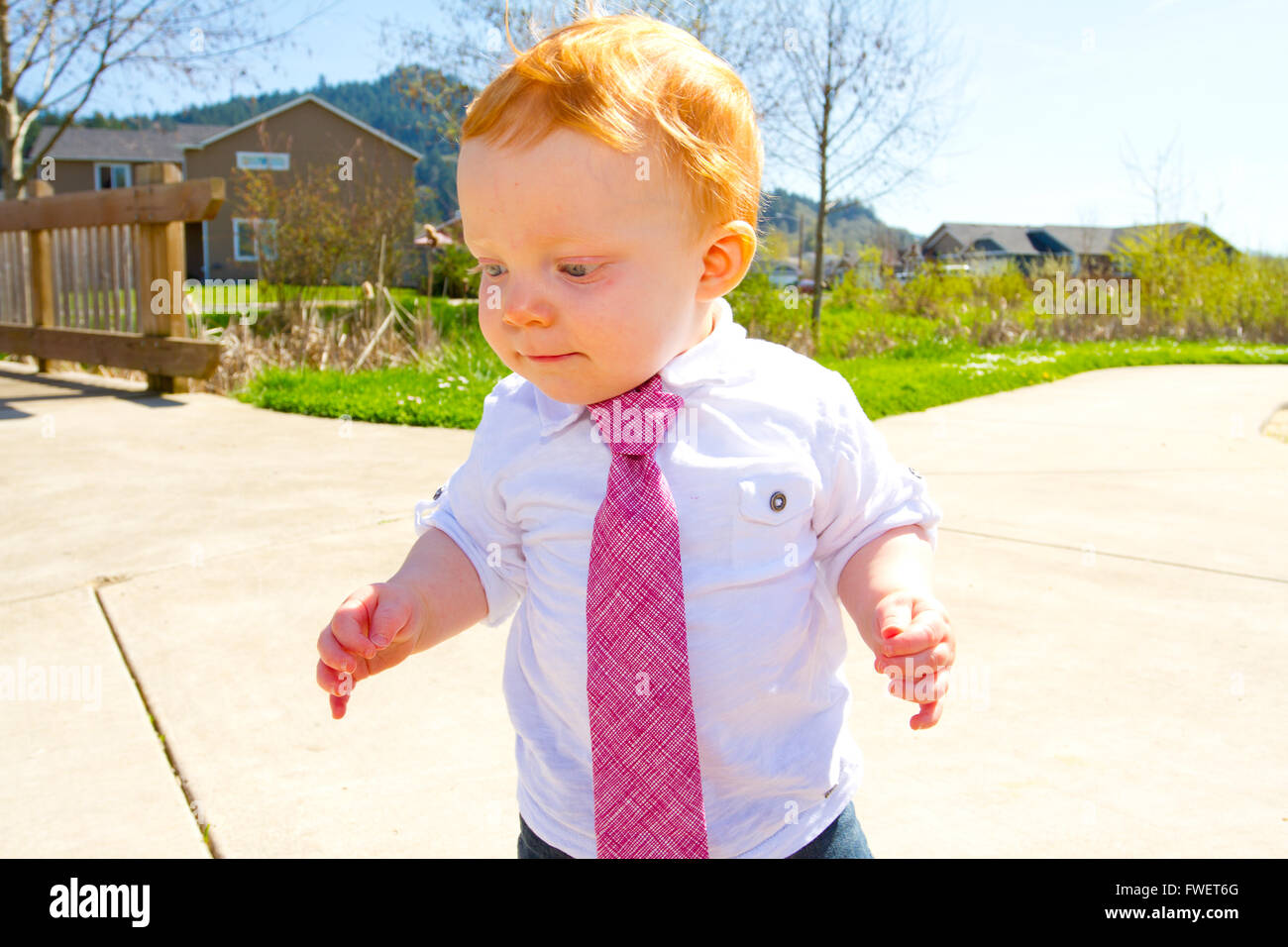 A baby boy plays at the park wearing his Sunday's best clothes including a tie around his neck. Stock Photo