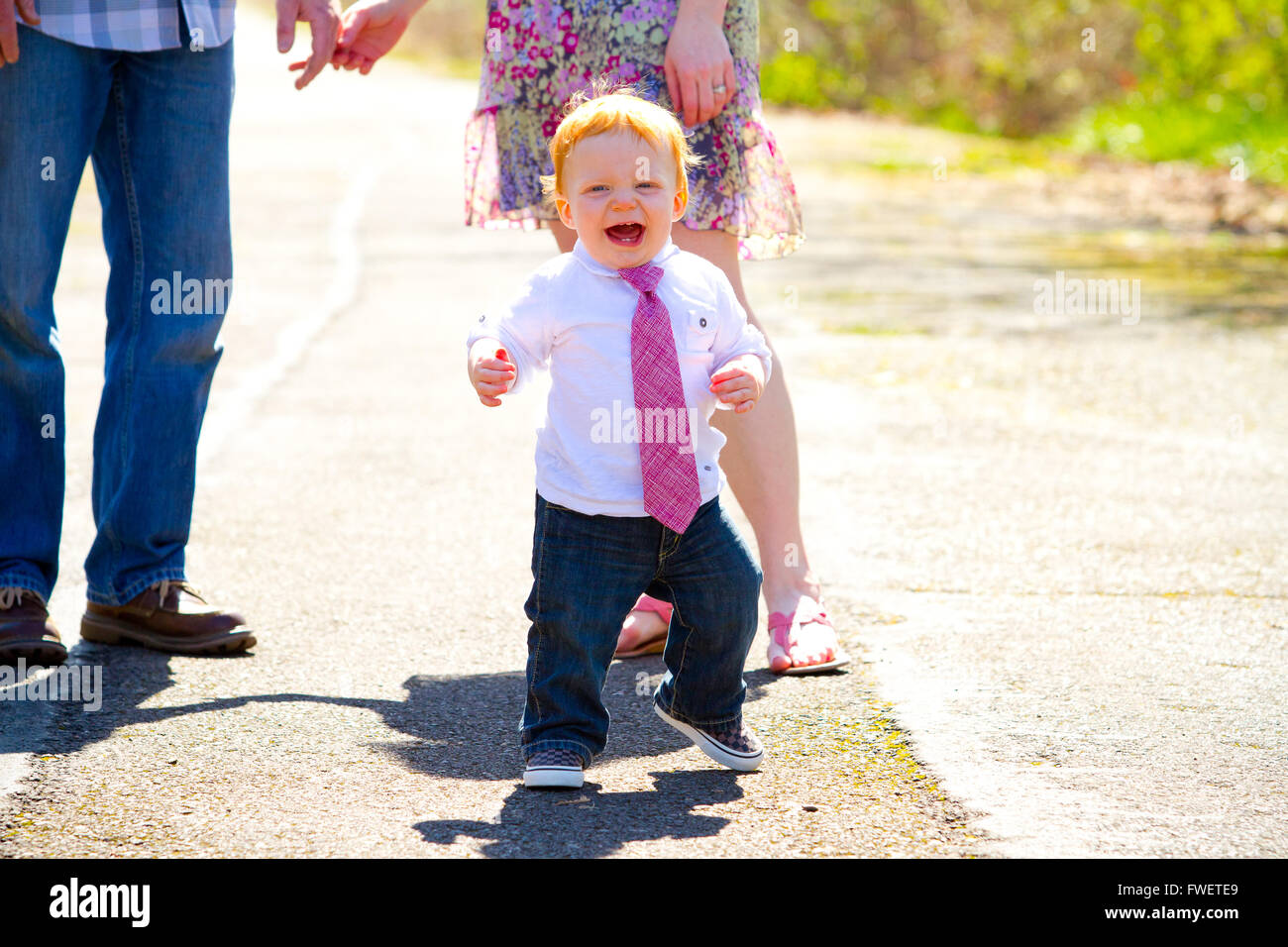 A baby boy runs away from his parents during an outdoor photo shoot with the family. Stock Photo