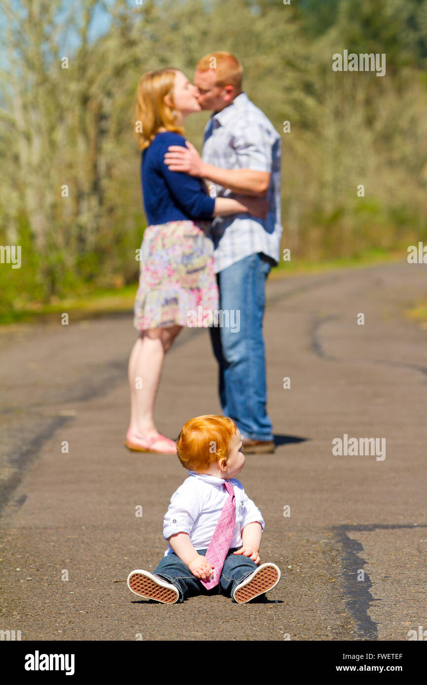 In this selective focus image the parents of a baby one year old boy are kissing out of focus in the background. Stock Photo