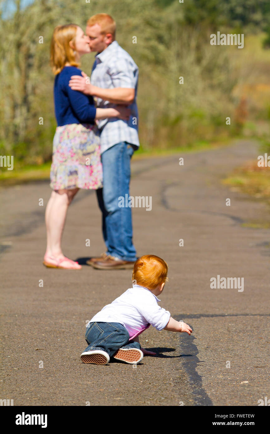 In this selective focus image the parents of a baby one year old boy are kissing out of focus in the background. Stock Photo