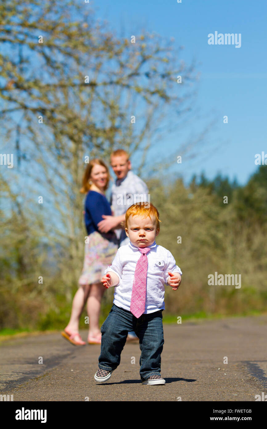 Parents are out of focus in this selective focus image while a baby boy runs toward the camera. Stock Photo